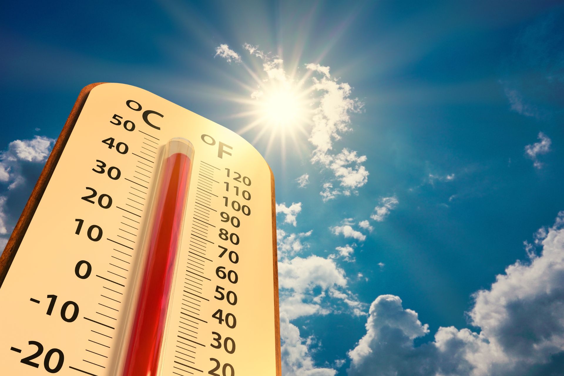 A thermometer showing a high temperature against a bright, sunny blue sky with scattered clouds.