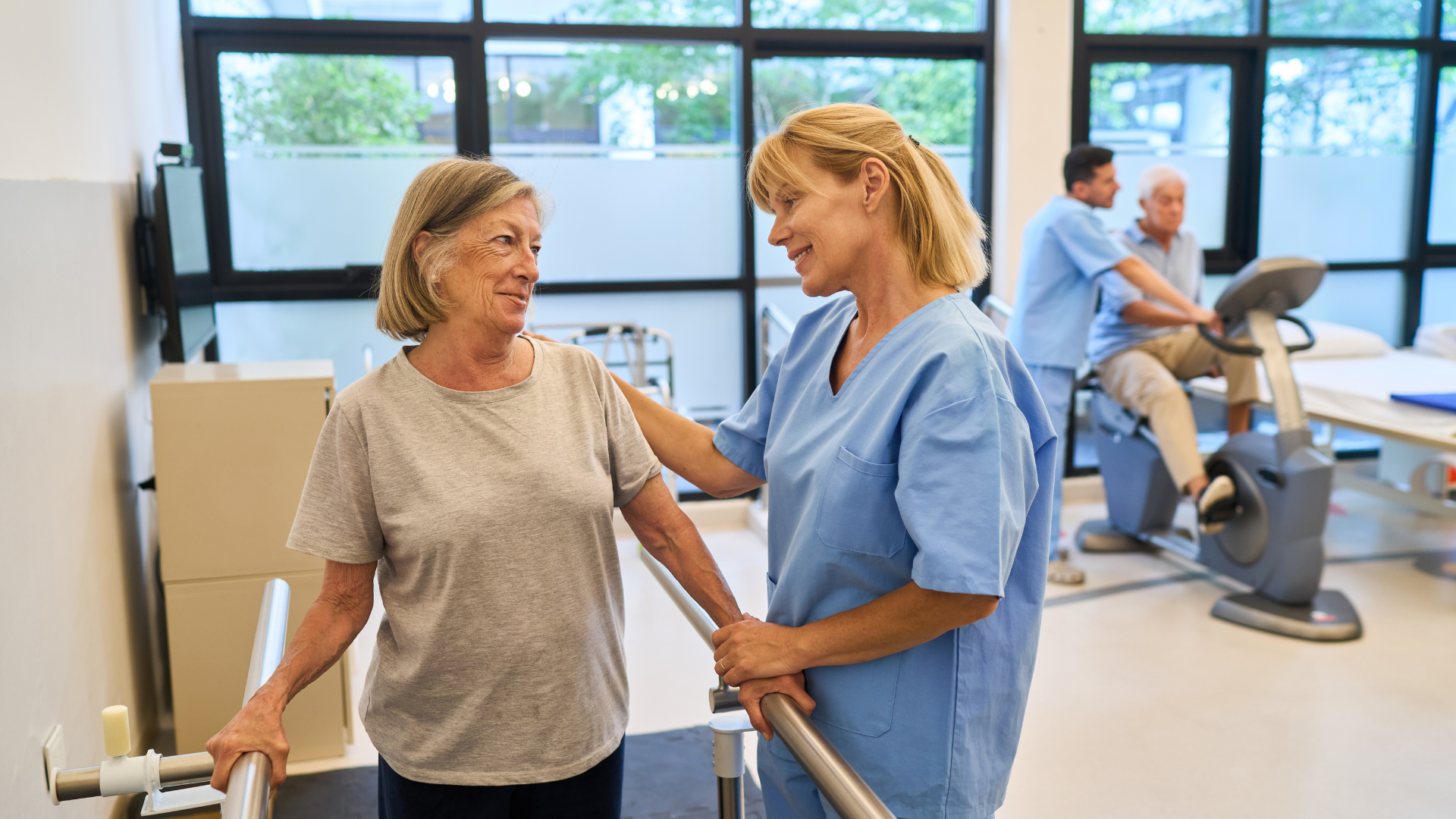 Physical therapist assisting a patient in a bright rehabilitation gym with exercise equipment nearby