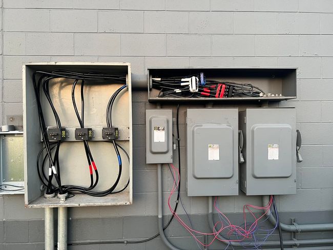 Electrical boxes on a gray brick wall. Wires and conduits connect the boxes, providing power.