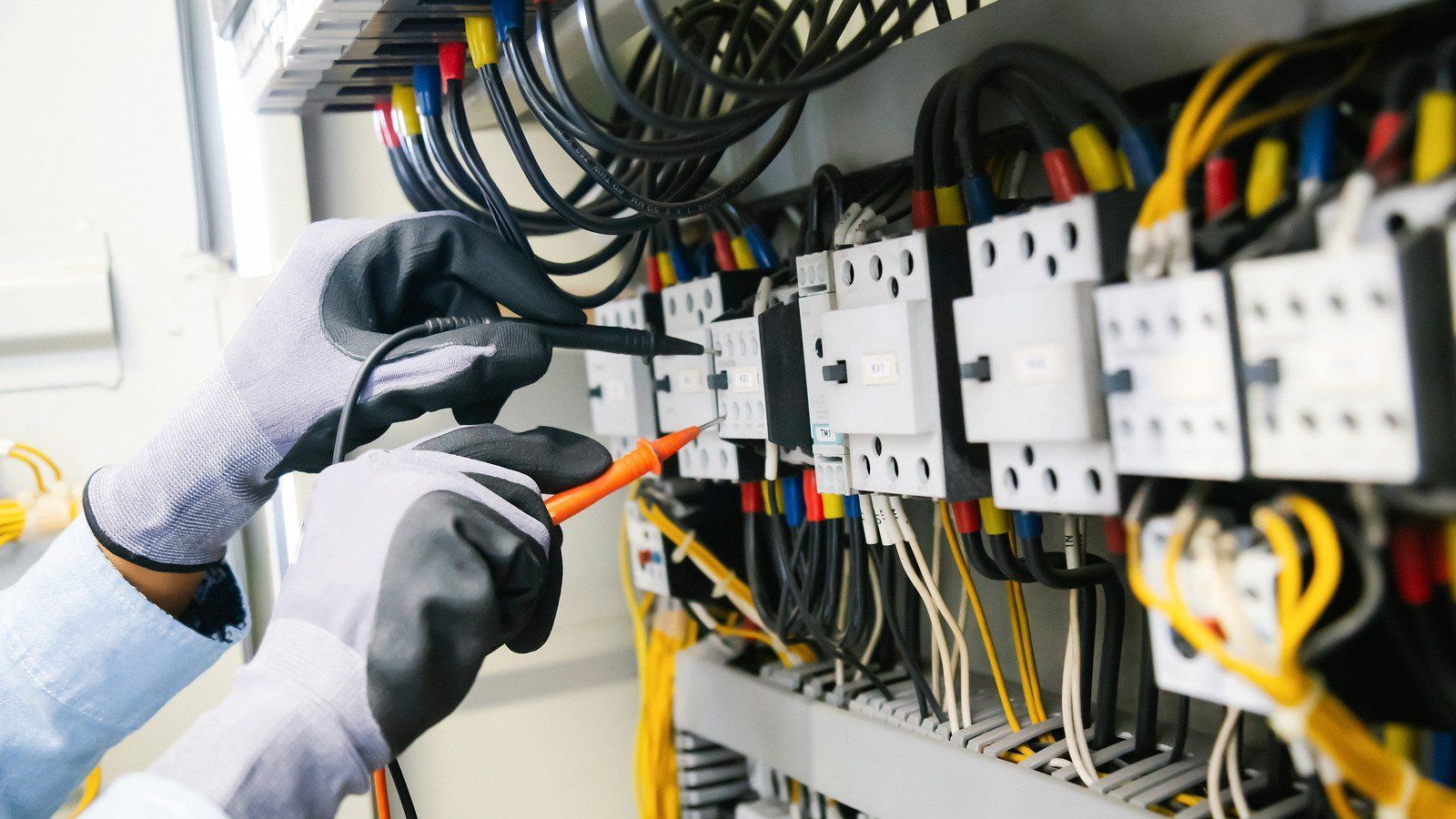 Gloved hands using a screwdriver to work on electrical control panels with wires and circuit breakers