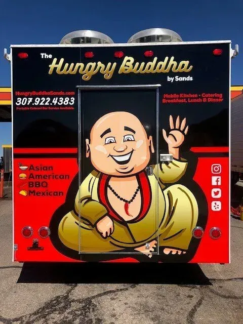 Food truck sign for “The Hungry Buddha,” black and red with a smiling cartoon Buddha mascot and Asian/American/BBQ menu text