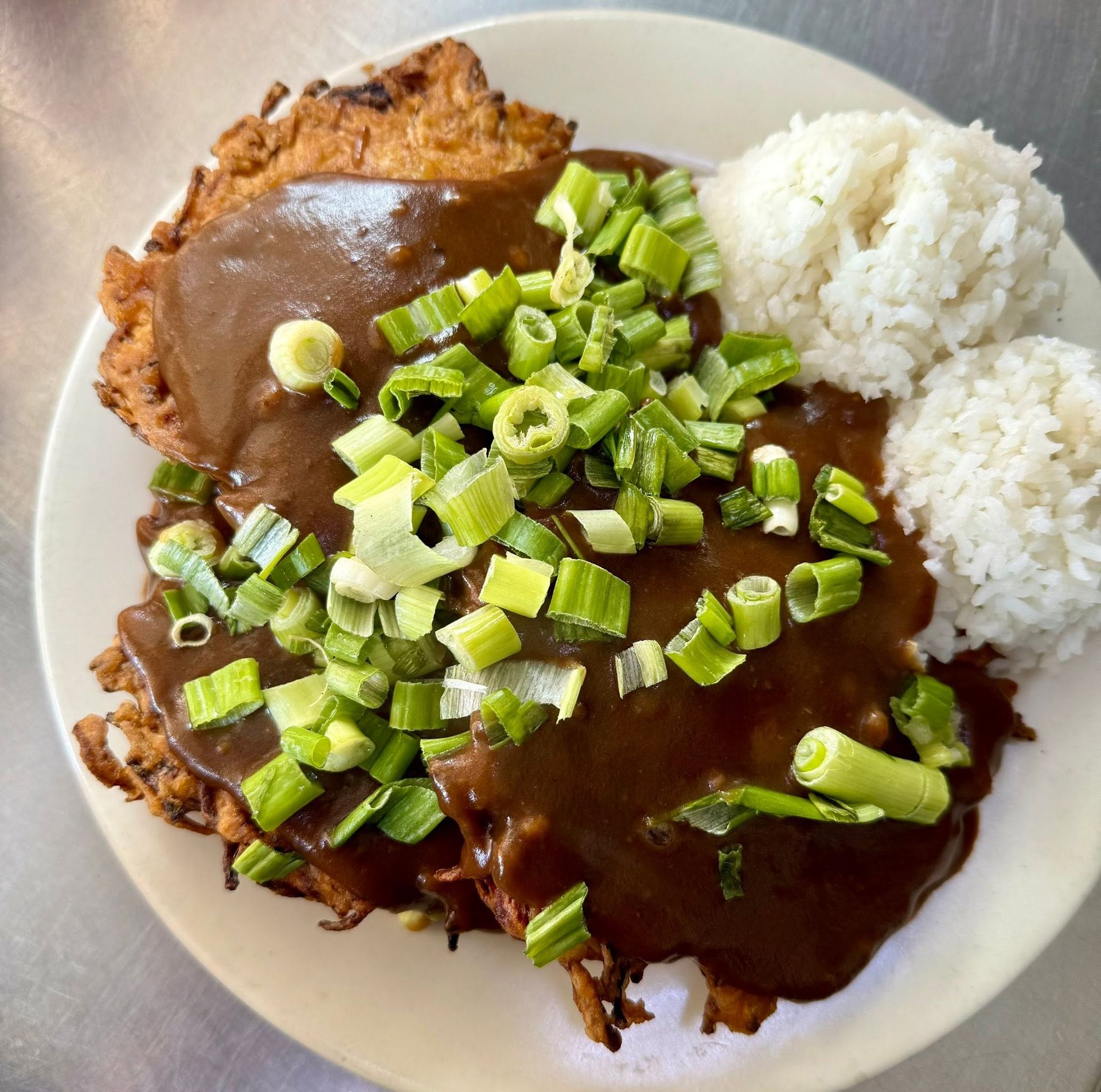 Plate of breaded meat topped with brown gravy and chopped green onions, served with white rice.