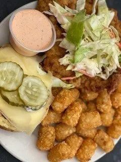 Plate of fried food with coleslaw, pickles, sauce, and hush puppies on a white plate