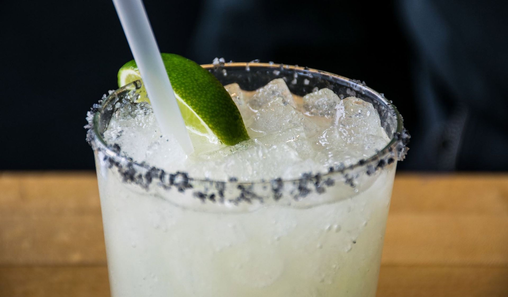 Frosty margarita with a salted rim, lime wedge, and straw on a wooden table