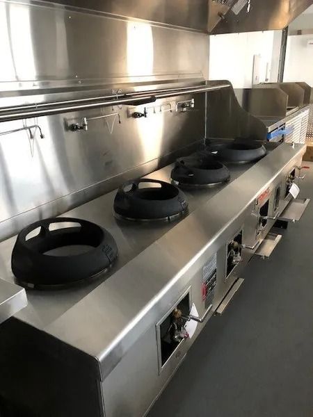 Stainless steel commercial kitchen stove with four burners and ventilation hood