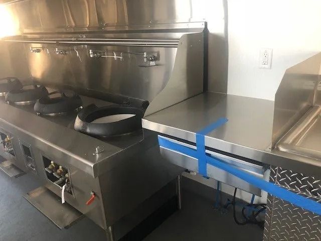 Commercial kitchen with stainless steel stovetop and countertop, blue tape marking a service area