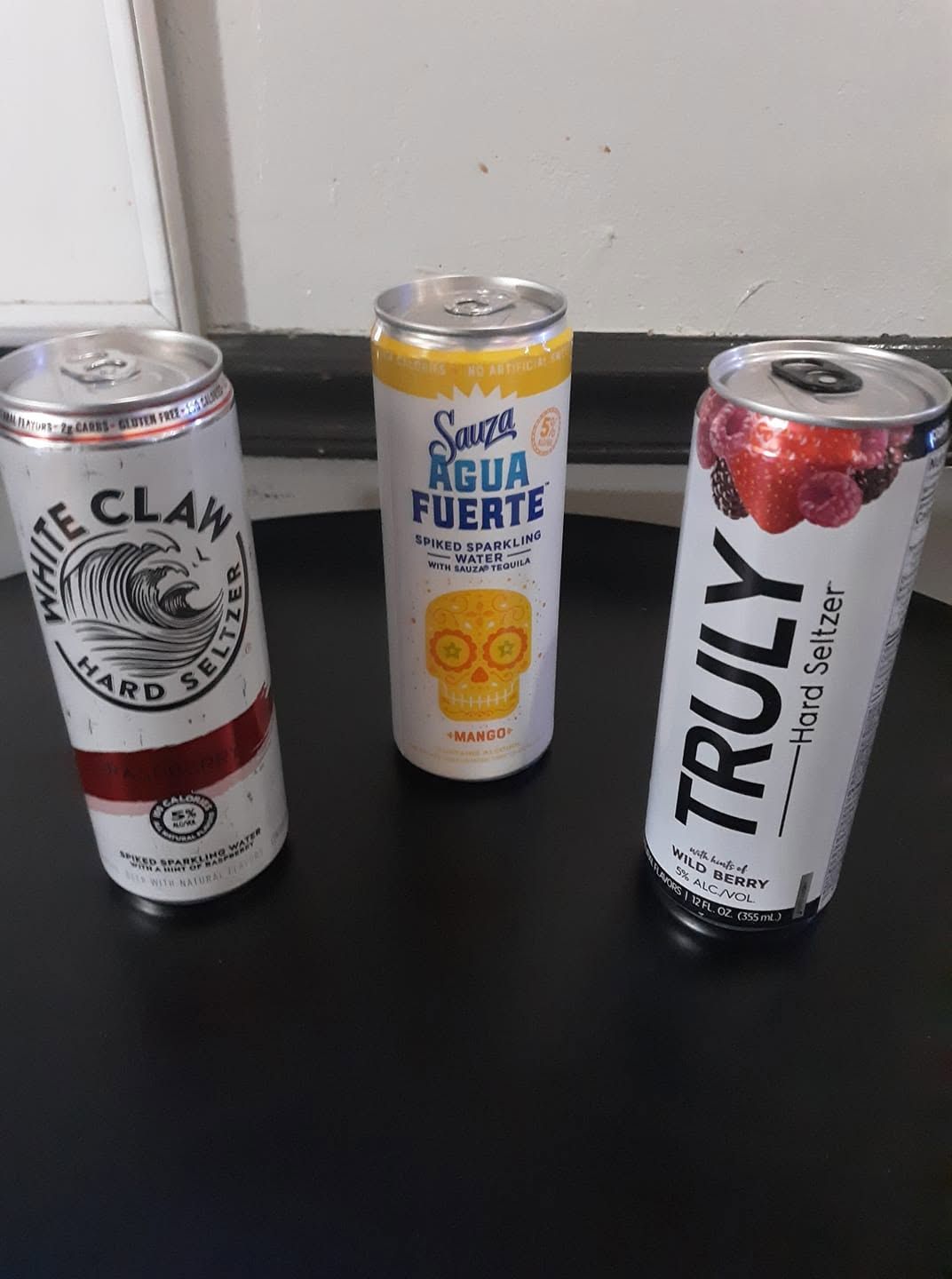 Three sparkling water cans on a black table, including White Claw, San Pellegrino, and Truly.