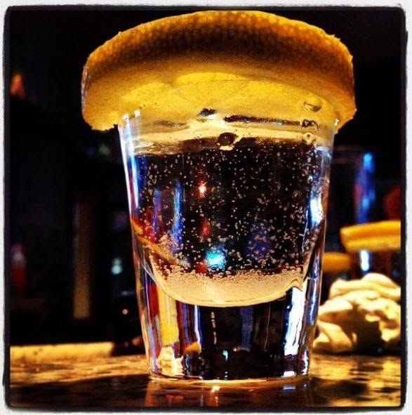 A salted shot glass with clear liquid on a bar counter, lit warmly against a dark background.