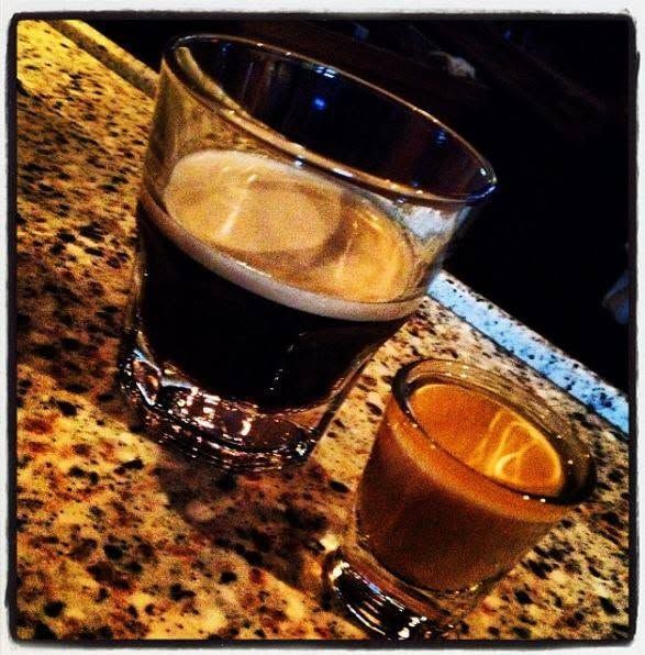 Two espresso shots in small glasses on a speckled countertop, one dark and one amber.