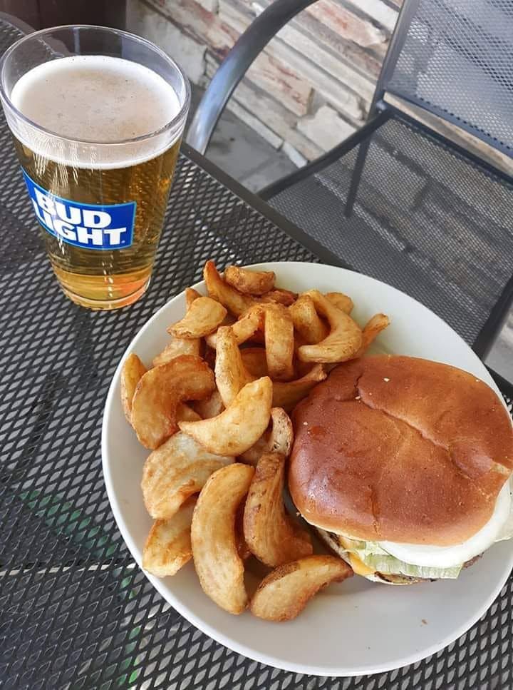 Burger and fries on a white plate beside a Bud Light beer on a metal patio table.