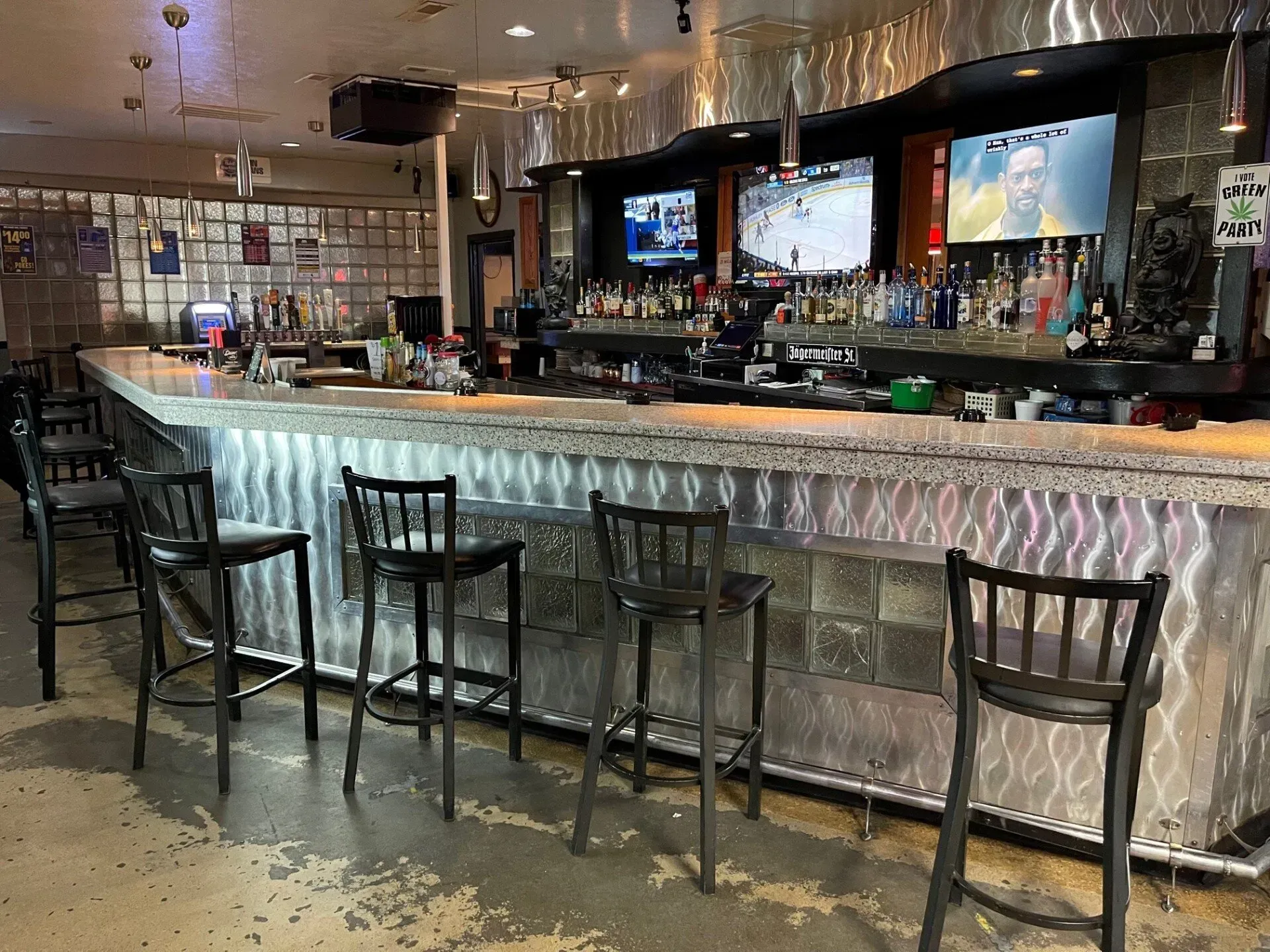 Modern bar interior with illuminated counter, stools, TVs, and hanging glass racks