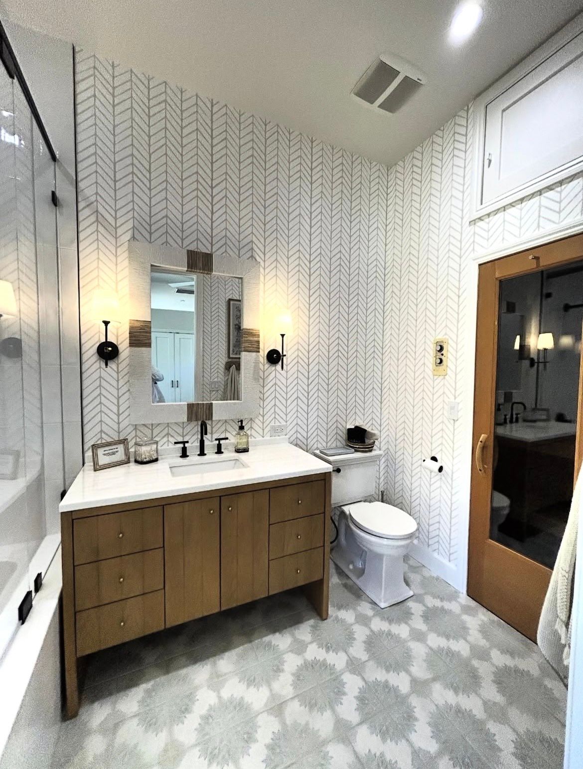 Bathroom with patterned wallpaper, wood vanity, and floral tile flooring.
