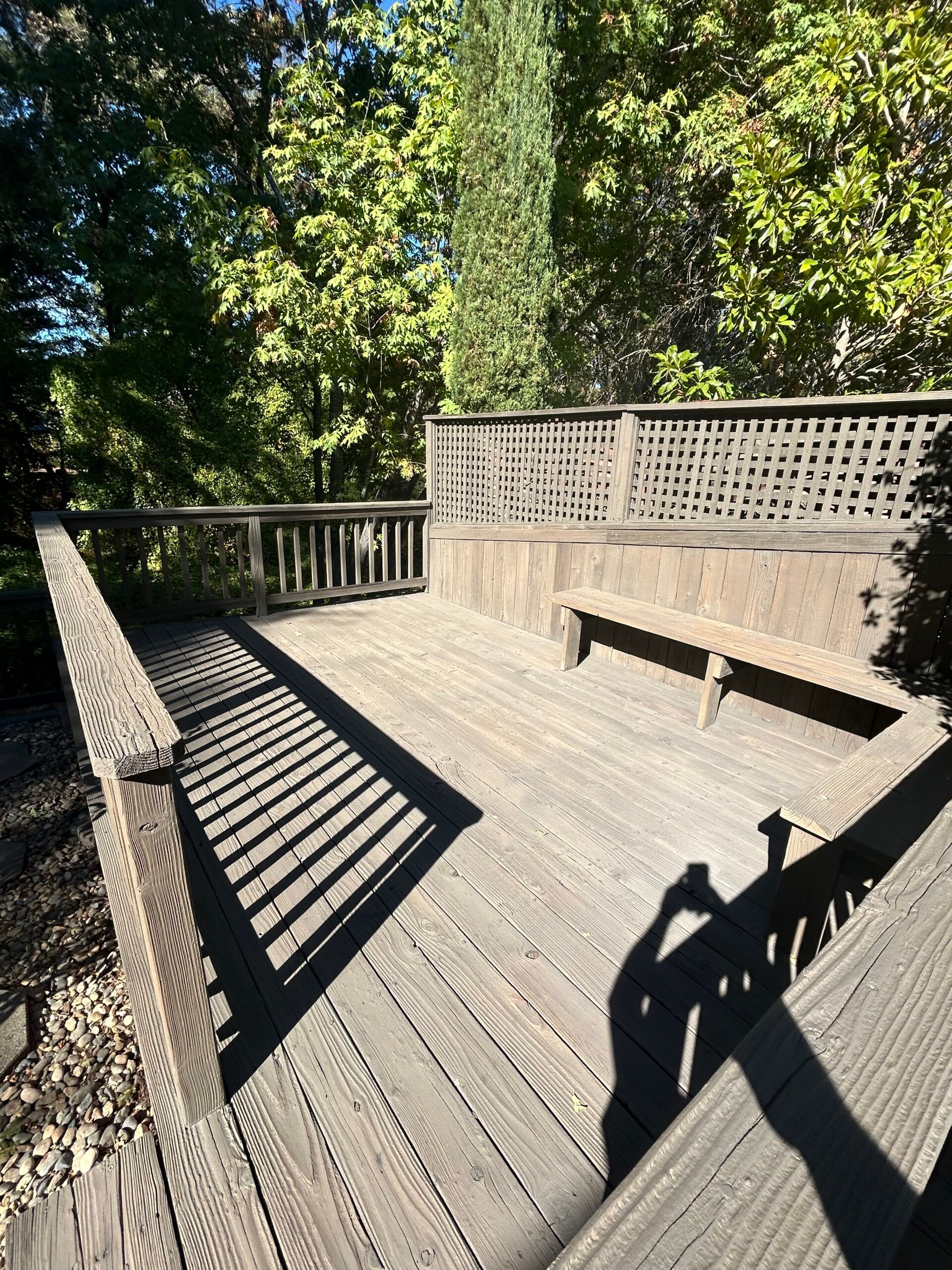 Wooden deck surrounded by greenery, with a bench and decorative railing.