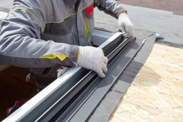 Trabajador instalando paneles de techo metálicos con guantes en una obra de construcción.