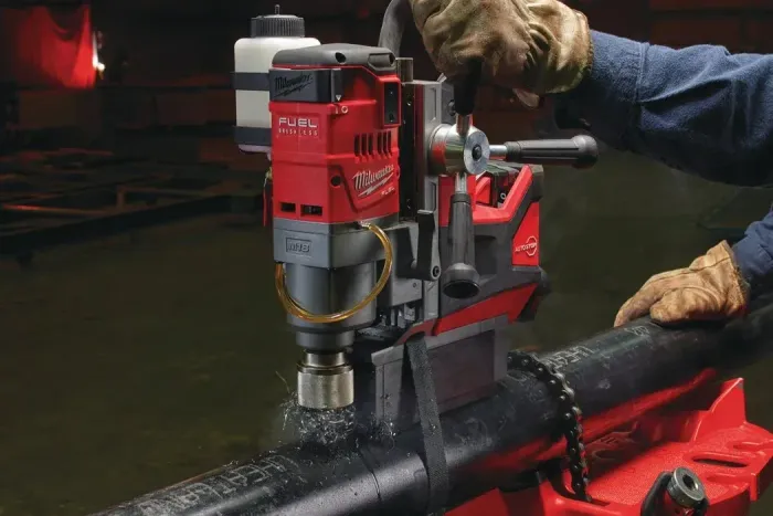 Un operaio con i guanti utilizza un trapano magnetico Milwaukee per praticare un foro in un tubo di metallo.