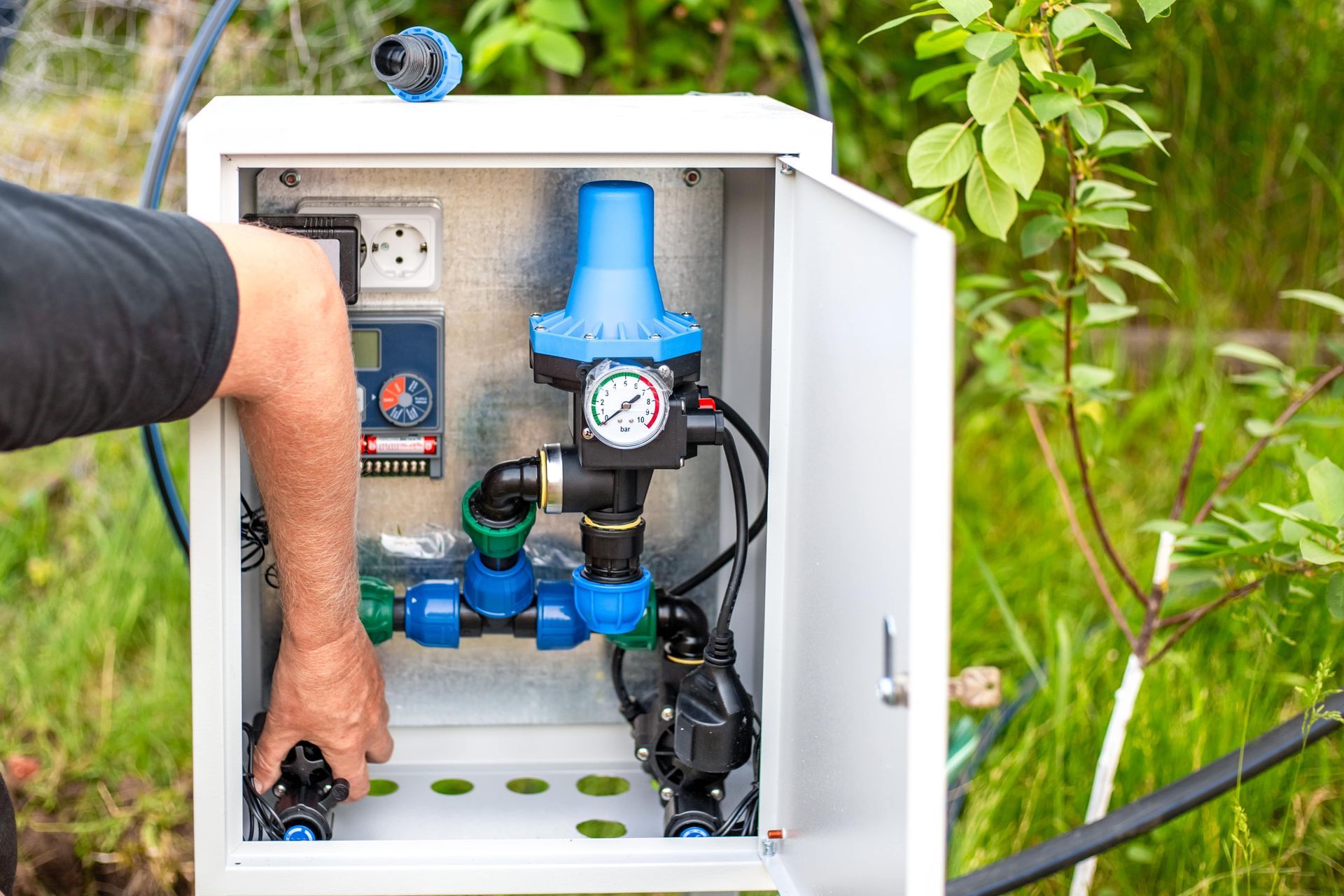 Open utility cabinet with water filter system and blue components being adjusted by a hand