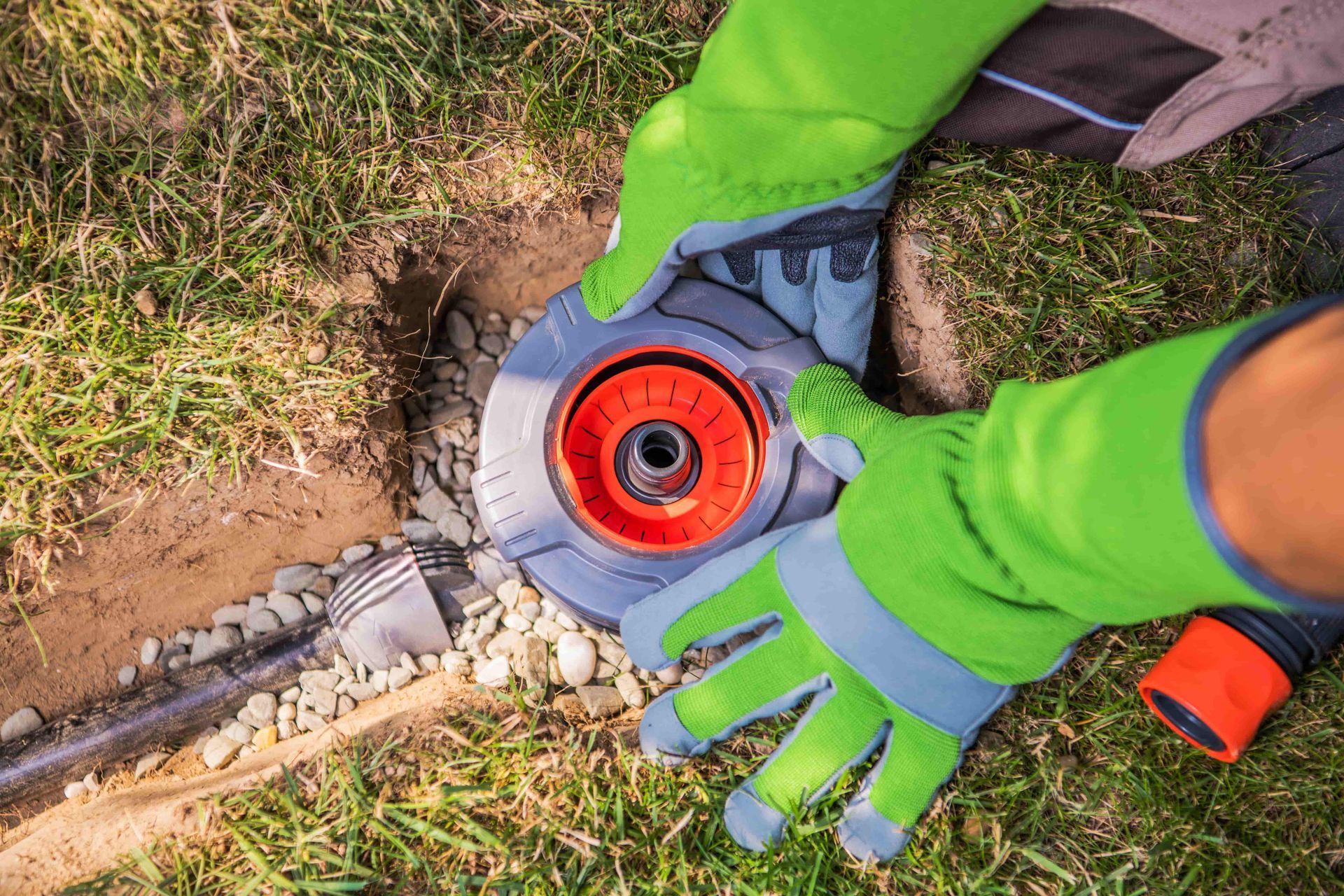 Gloved hands adjusting a red chainsaw on grass and dirt outdoors