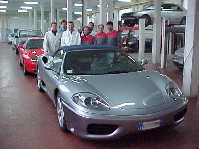 Un gruppo di persone in piedi attorno a un'auto sportiva color argento