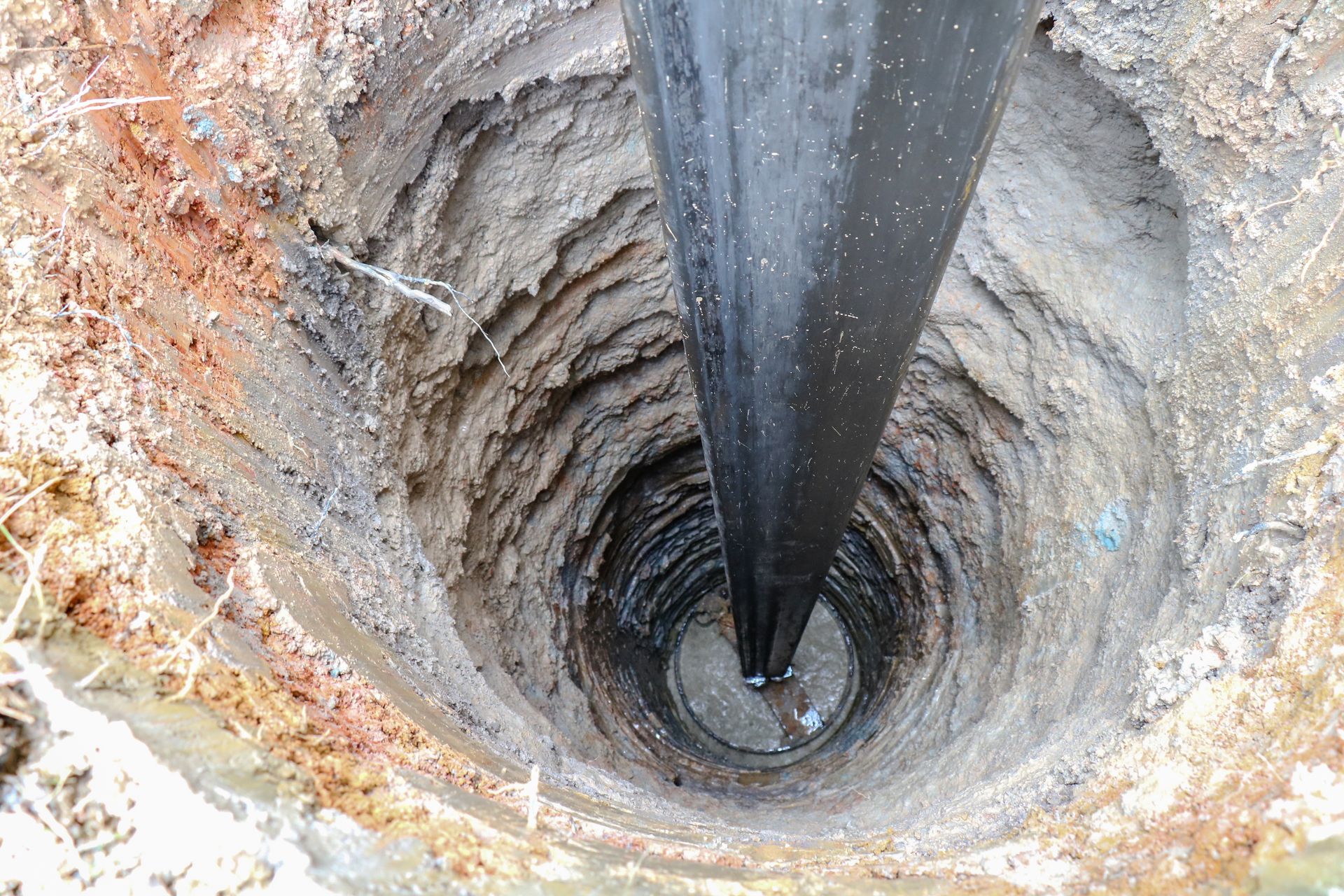 A view looking down into a deep water well with a pipe extending into wet soil layers.