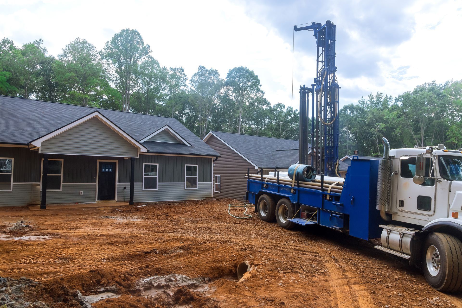 A water well drilling rig truck parked at a residential construction site with exposed red clay soil