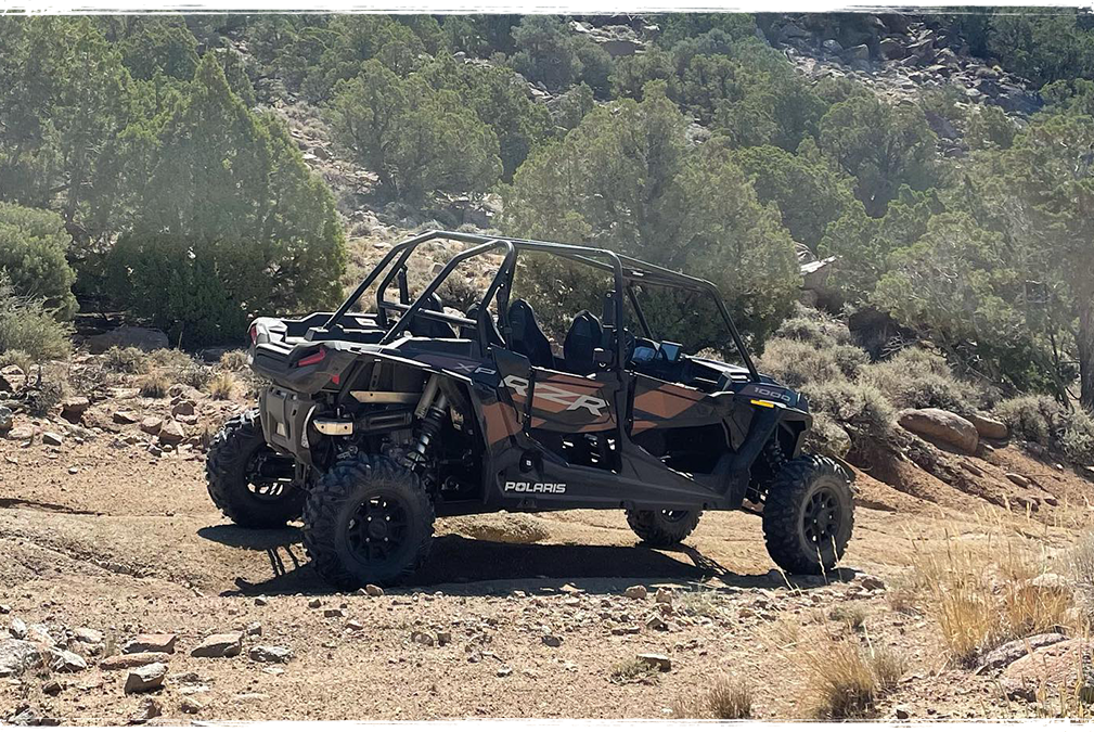black and white Polaris RZR UTV on sandy trail in desert leaving dust behind