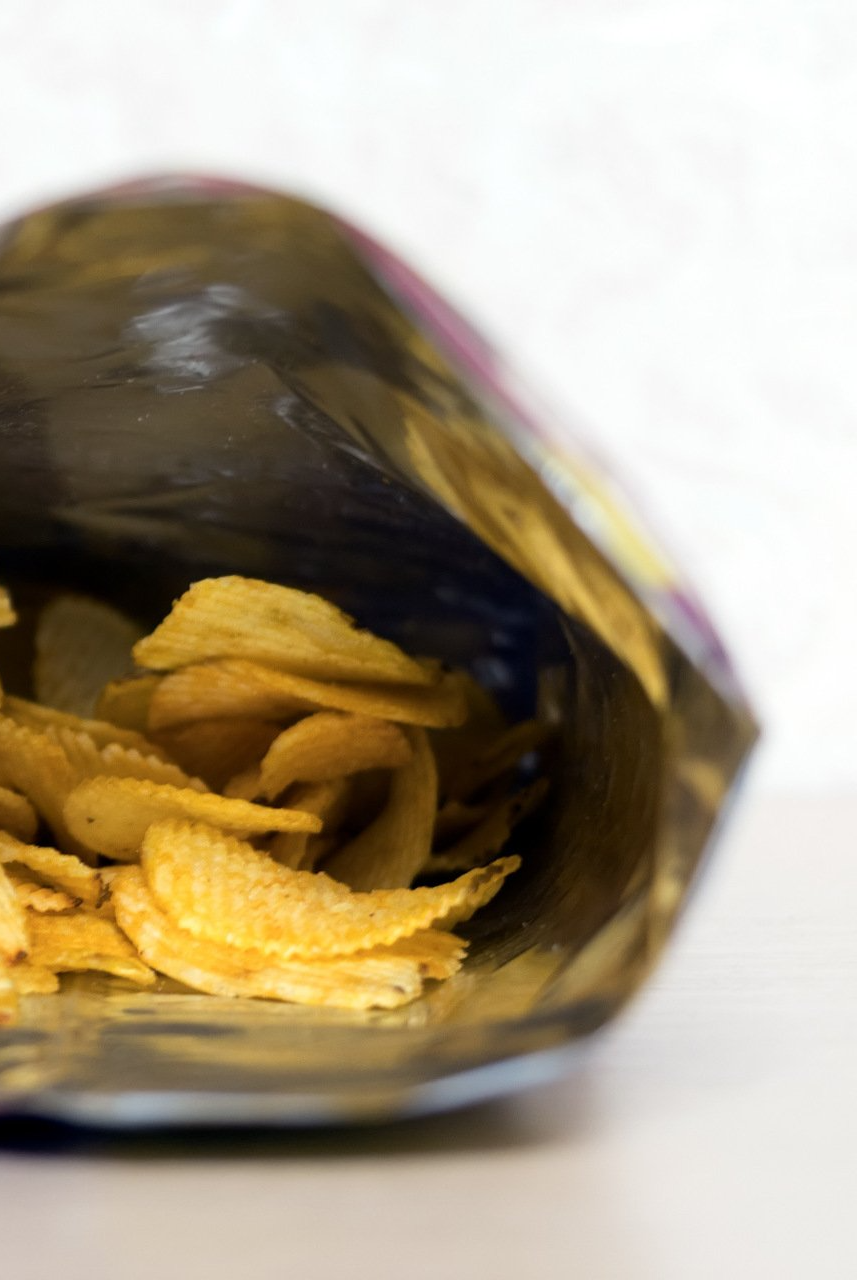 An open bag of golden, crispy potato chips sitting on a white surface.