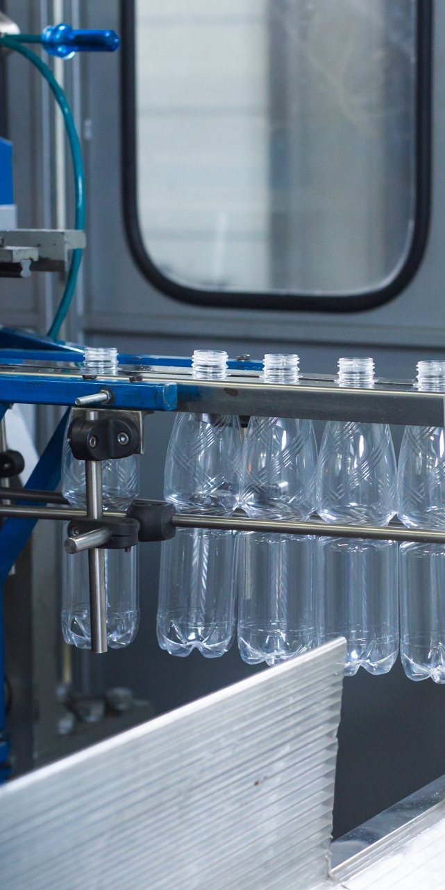 Clear plastic bottles moving along a metallic industrial production conveyor line.