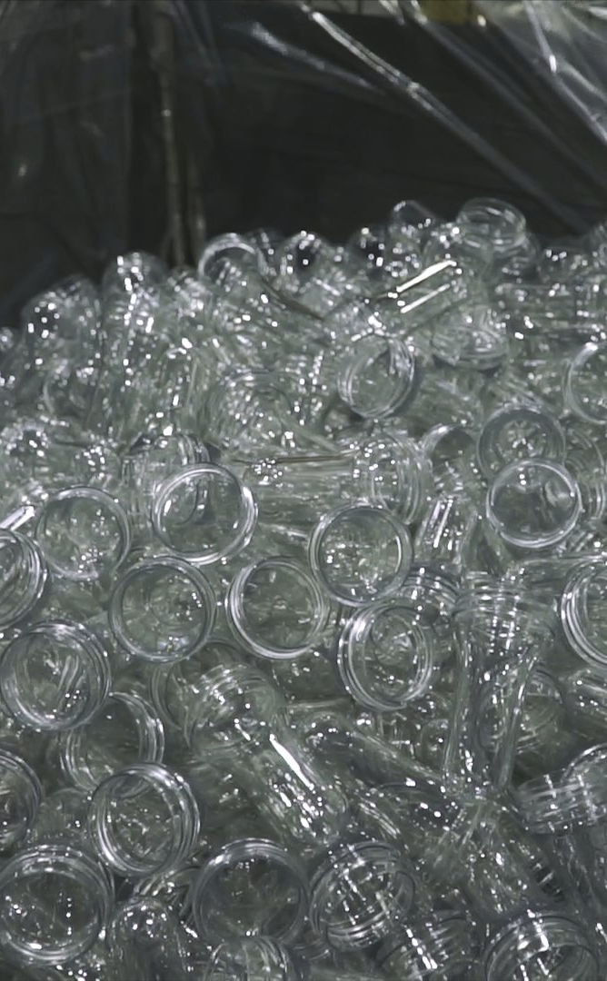 A large pile of clear, hollow plastic PET preforms used for manufacturing bottles.