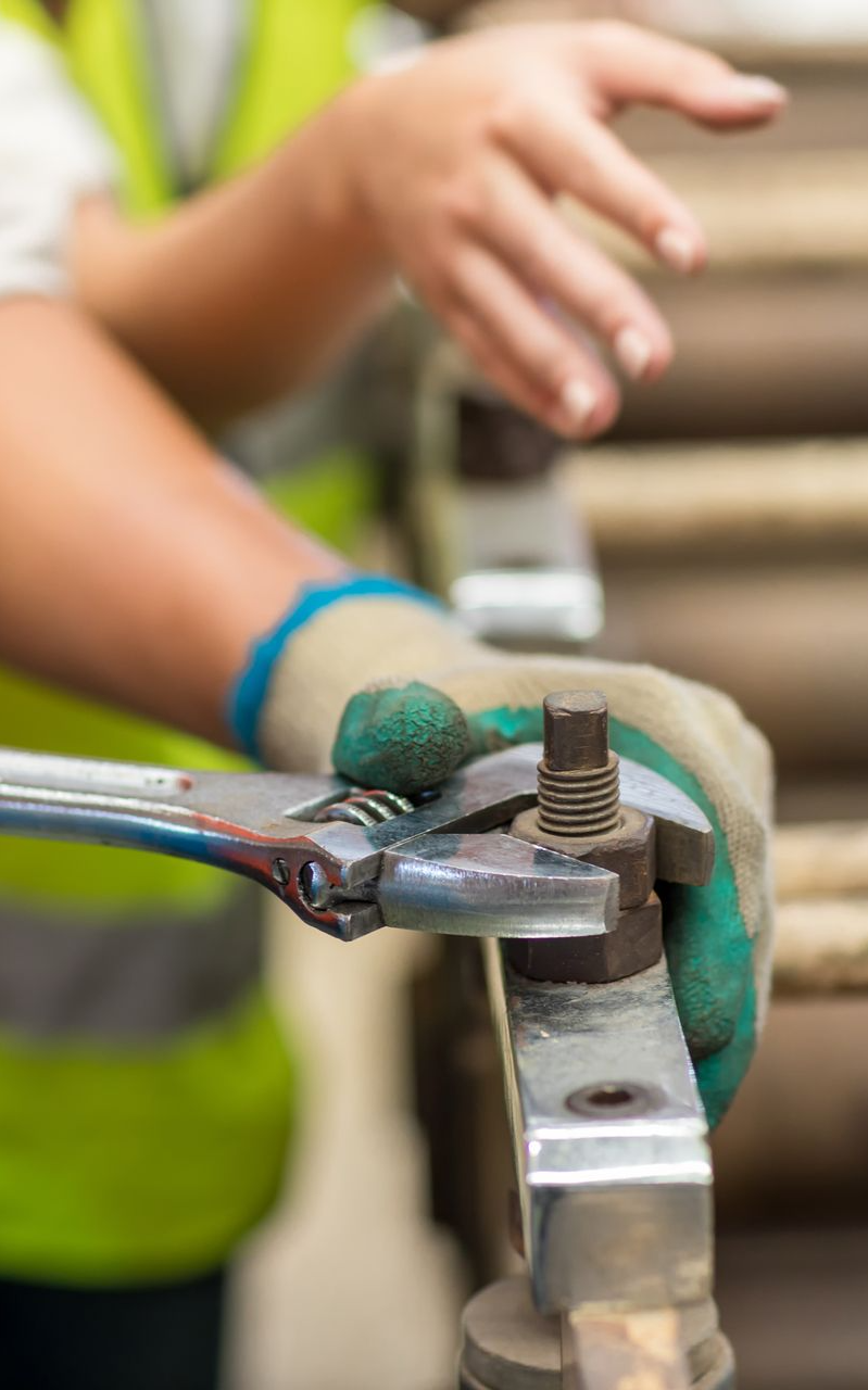 A worker in a high-visibility vest uses an adjustable wrench to tighten a metal nut on a piece of machinery.
