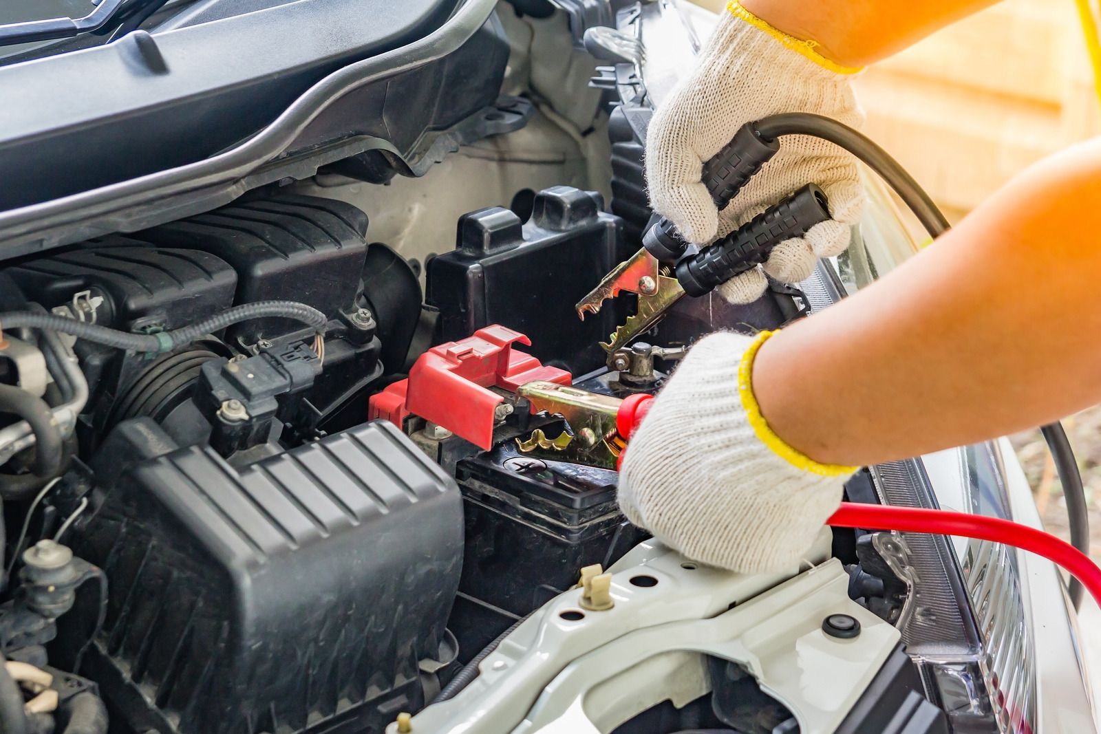 Person wearing gloves connecting jumper cables to a car battery.