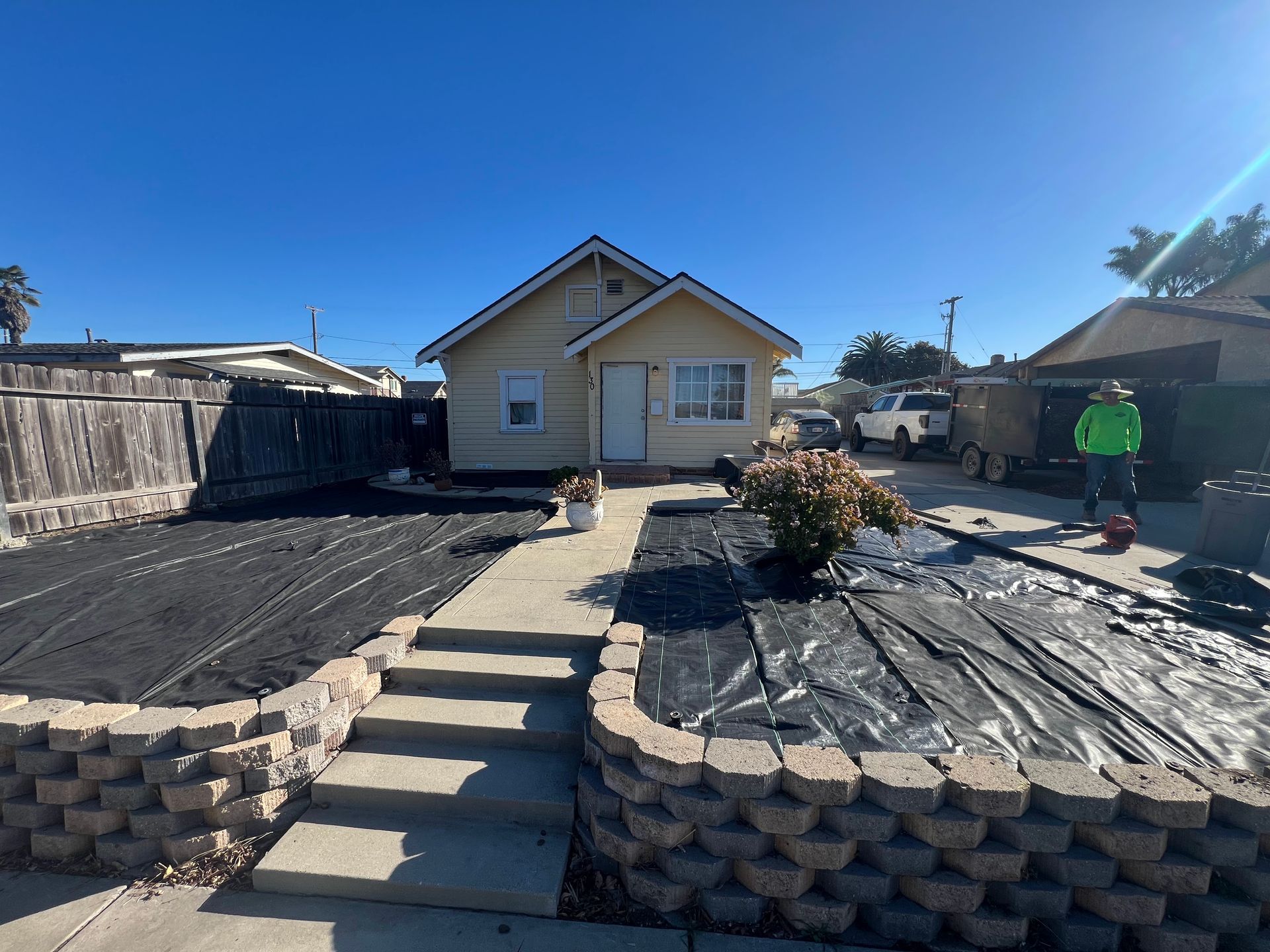 A small yellow house with a new front yard landscaping, under a blue sky.