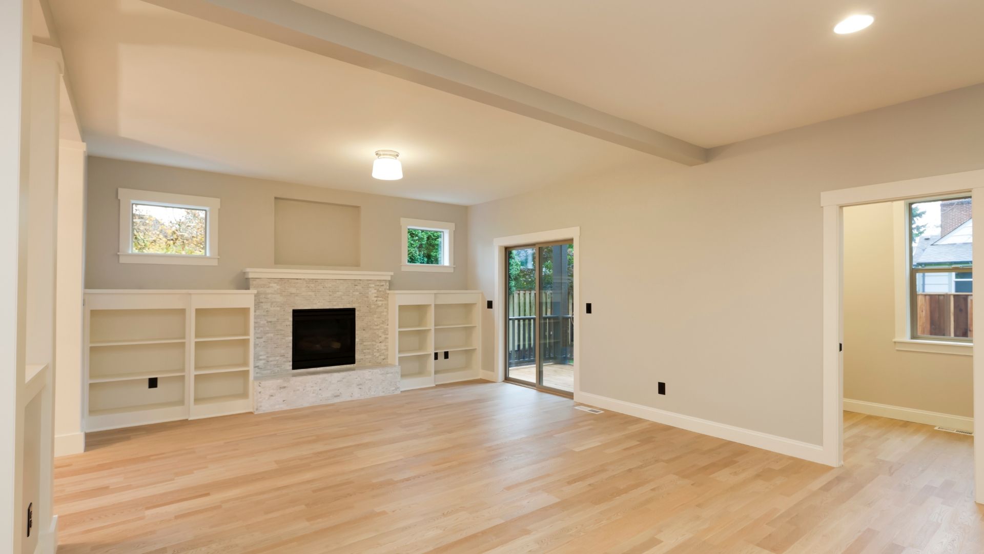 Empty living room with light wood floors, white fireplace, built-in shelves, and a doorway to another room