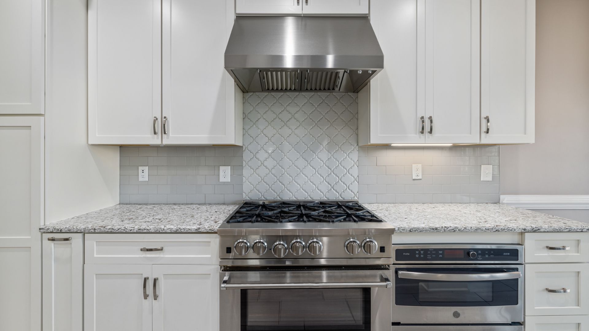 Modern kitchen with white cabinets, gray tile backsplash, granite counters, and stainless steel stove and range hood