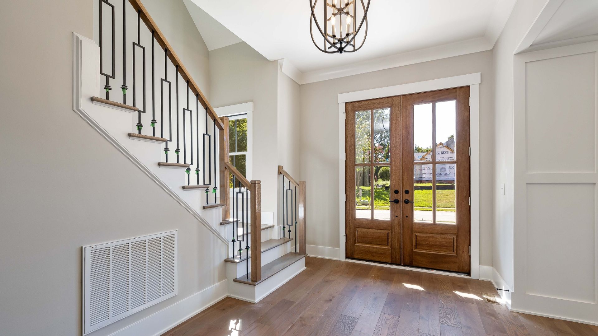 Bright foyer with wooden front doors, staircase, white walls, and hardwood floor