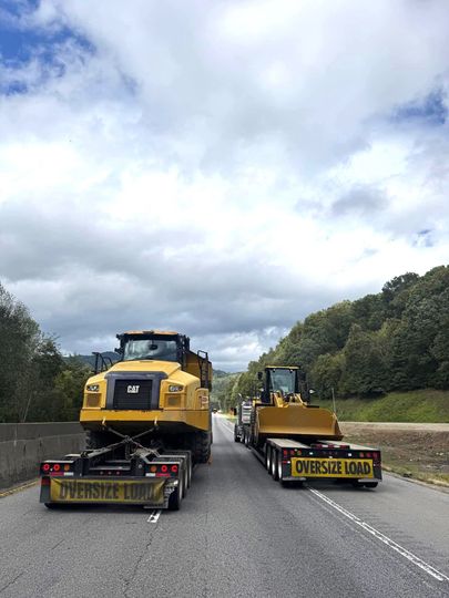 Two tractors are driving down a highway next to each other.