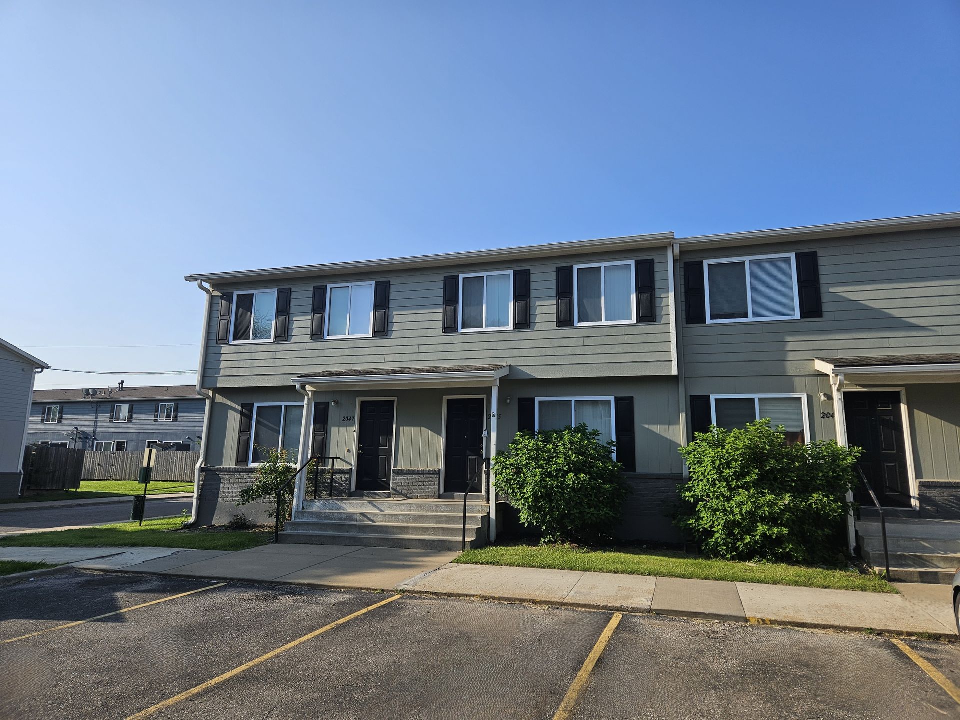 Townhouse exterior with grey siding, dark shutters, and a clear blue sky.