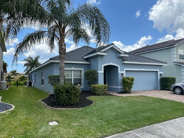 Blue house with a palm tree, green lawn, and blue sky.
