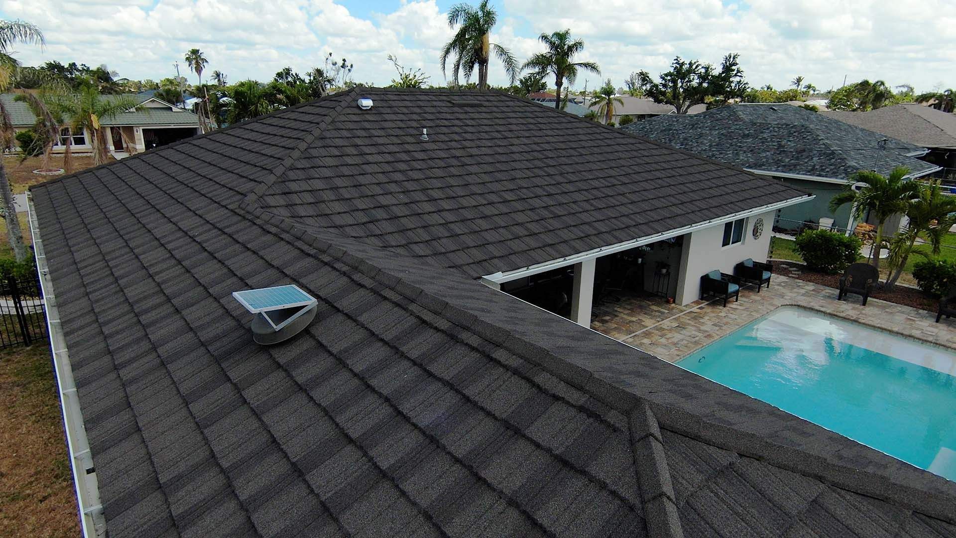 Dark gray shingle roof of a house with a pool, palm trees, and sunny blue sky.