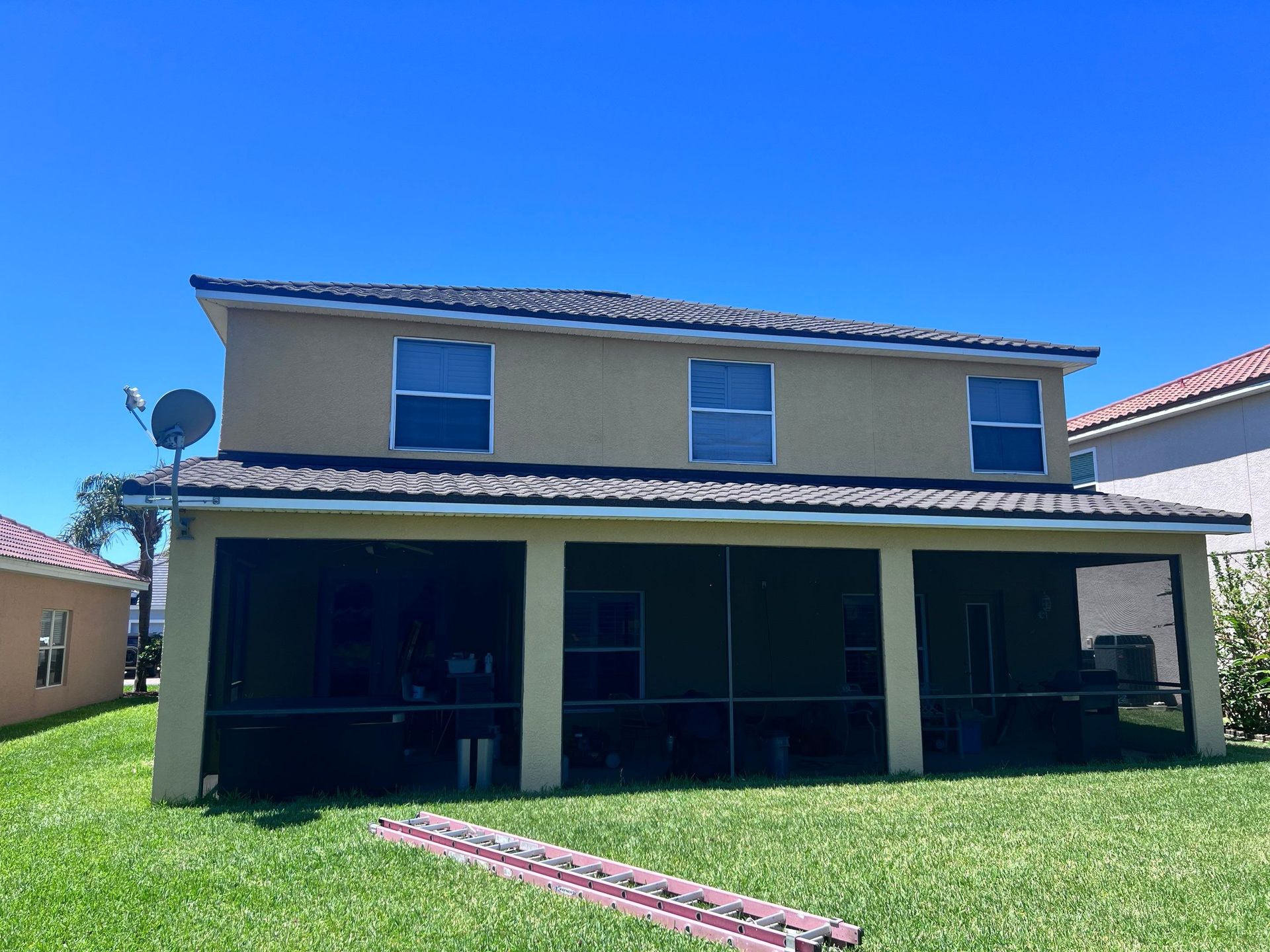 Two-story tan house with screened-in patio, green lawn, blue sky.