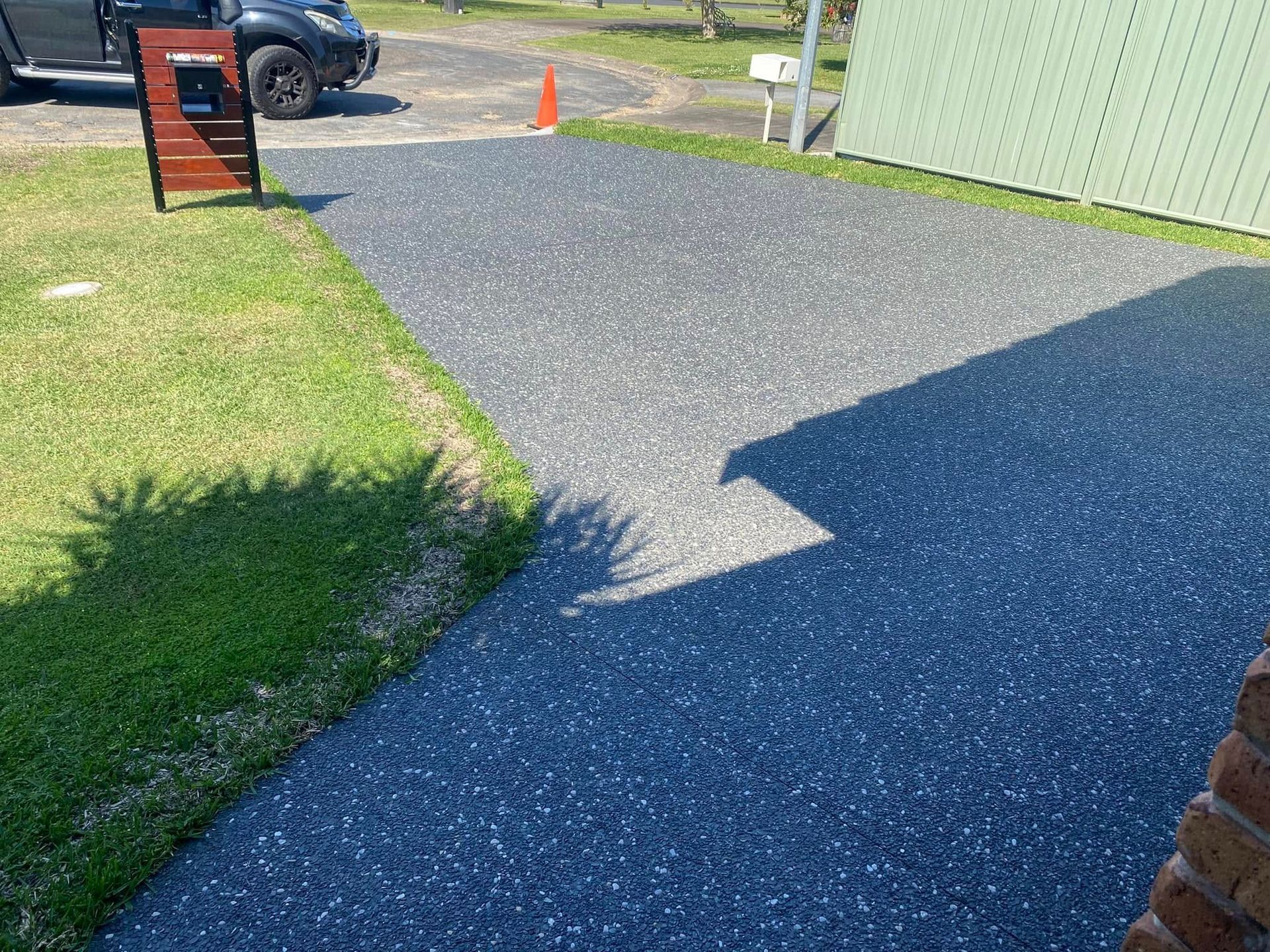 Dark grey speckled driveway with a car parked nearby, beside a green lawn and fence — Rhyno’s Concreting In Old Bar, NSW