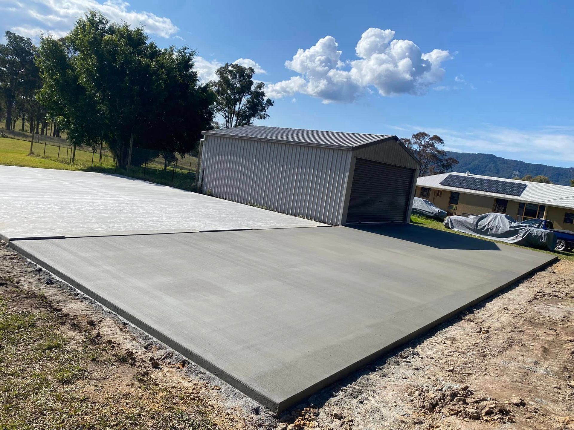 Newly poured concrete pad next to metal shed on a sunny day — Rhyno’s Concreting In Old Bar, NSW
