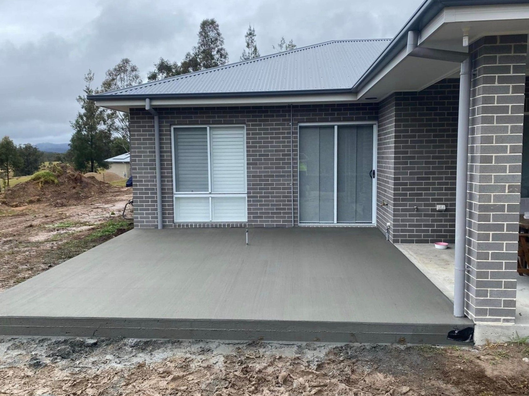 Newly Poured Concrete Patio Next to a Brick House — Rhyno’s Concreting In Old Bar, NSW
