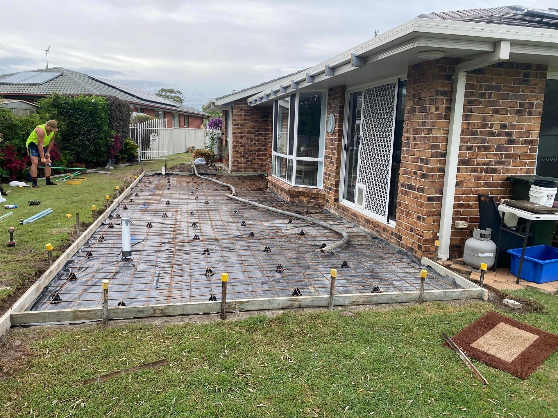 Concrete Patio Foundation Being Built Next to A Brick House; Worker on Lawn — Rhyno’s Concreting In Old Bar, NSW