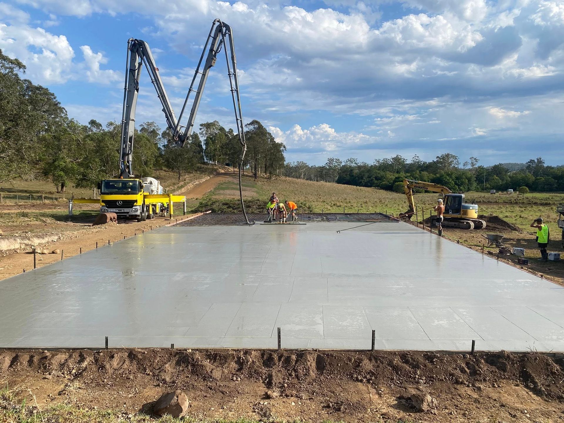 Newly poured concrete slab with metal shed, set against a hillside with blue sky and clouds — Rhyno’s Concreting In Old Bar, NSW