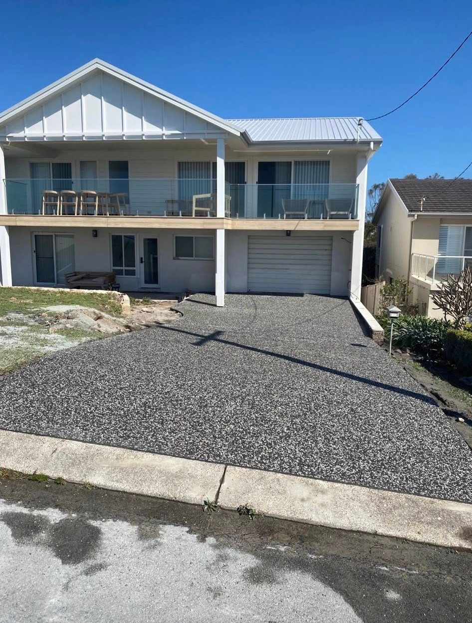 Two-story white house with gravel driveway, balcony, and garage on a sunny day — Rhyno’s Concreting In Old Bar, NSW