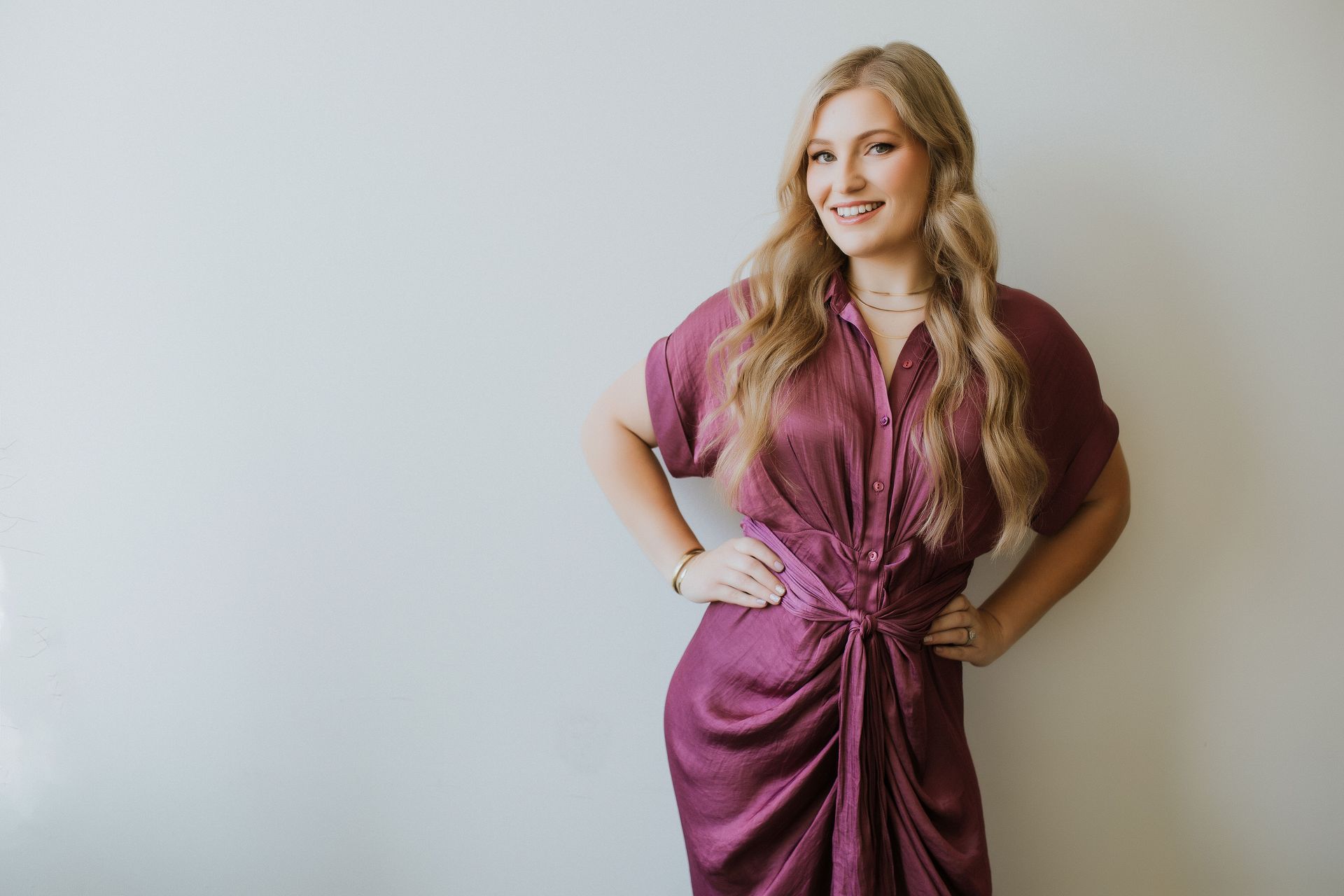 A woman in a purple dress is standing in front of a white wall.