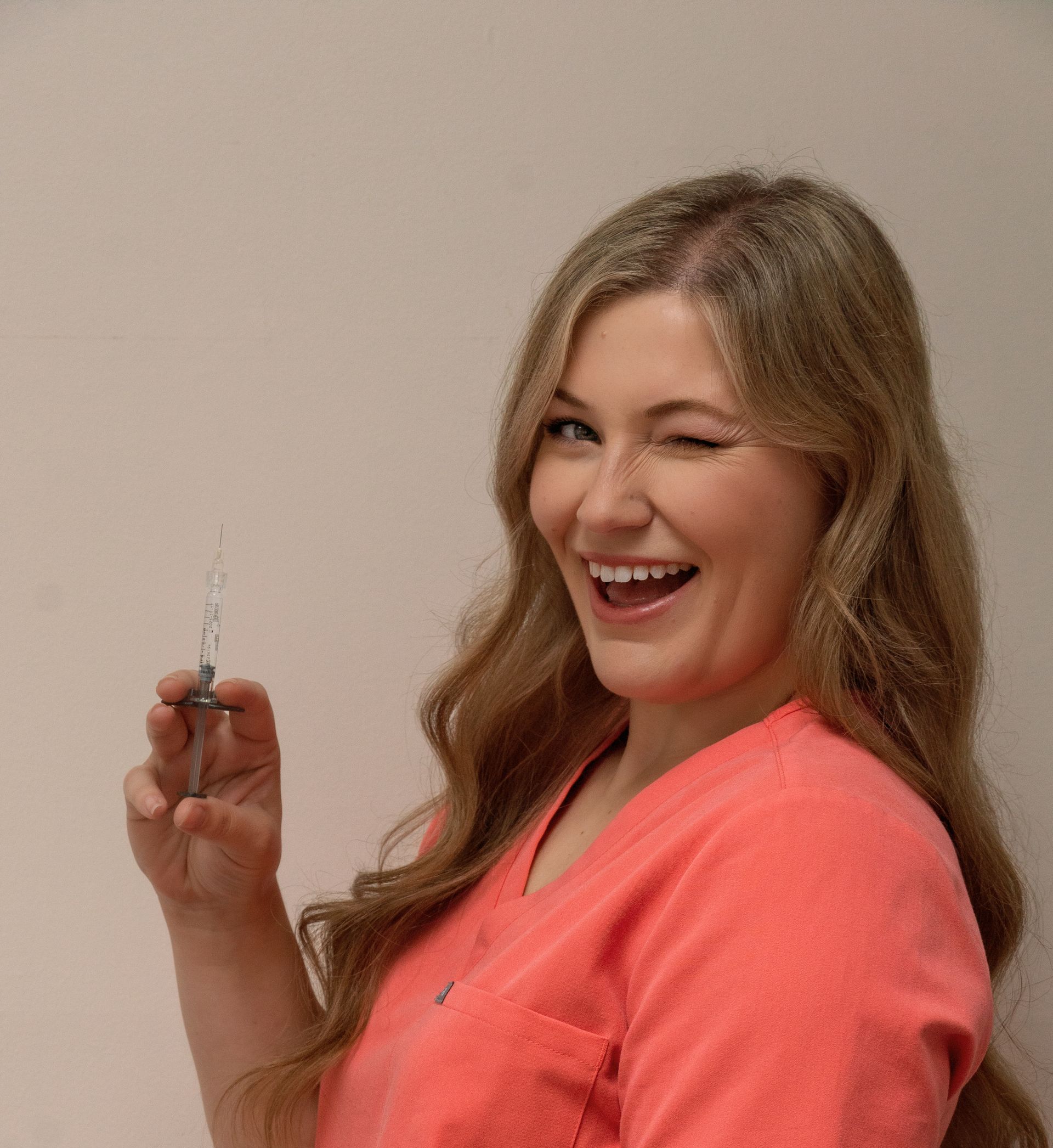 A woman in a pink shirt is holding a syringe and smiling.