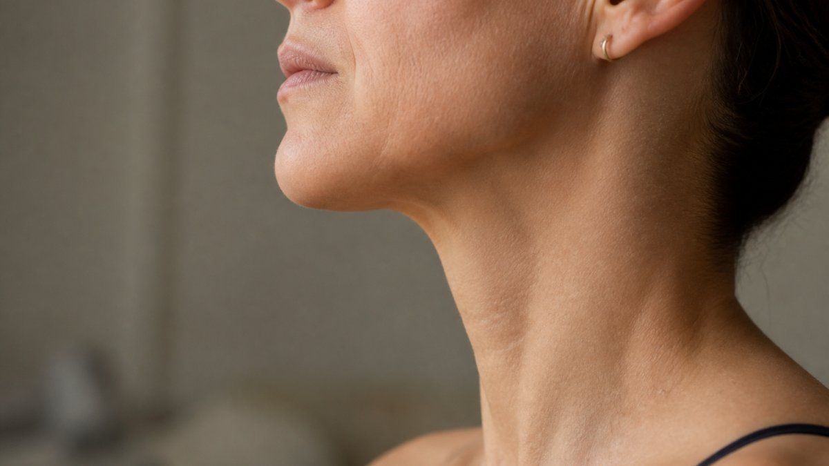 Close-up side profile of woman's neck and jawline showing muscle definition and contours with soft professional lighting