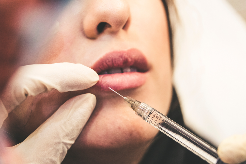 A woman is getting a botox injection in her lips.