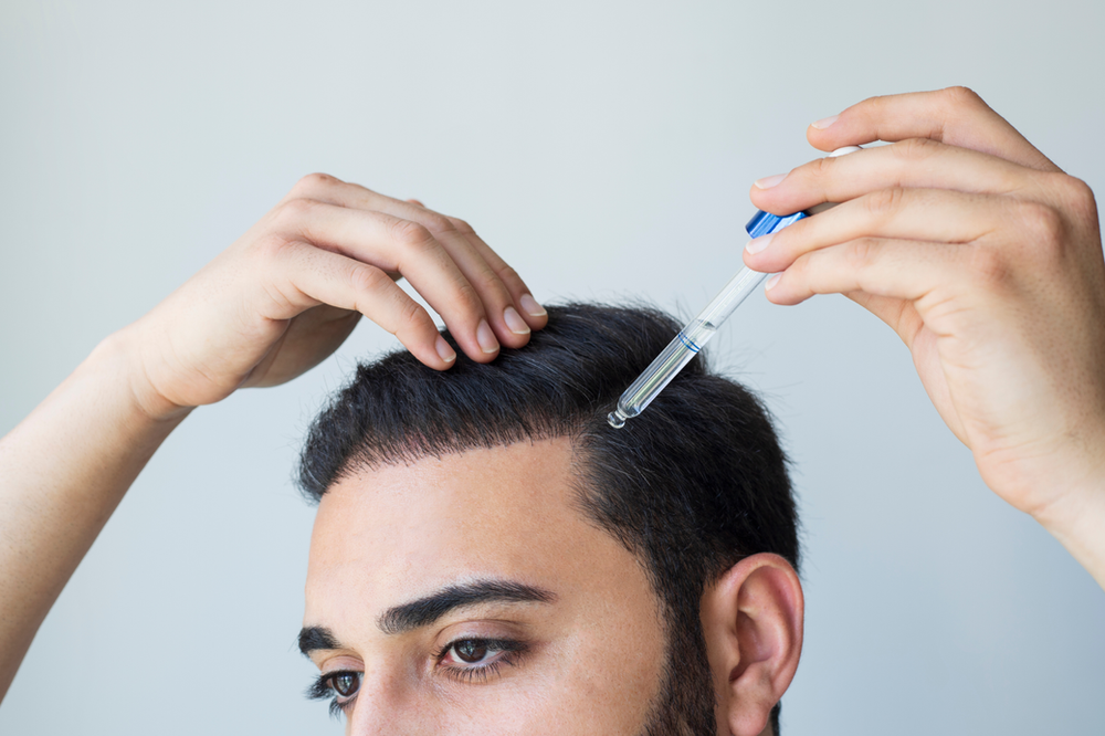 A man is applying a serum to his hair with a pipette.